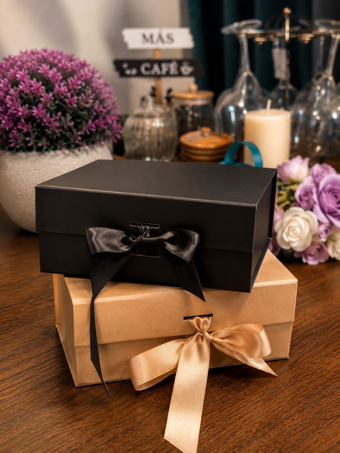 Two hand-wrapped Cozy Boxes with satin ribbon bows, styled with flowers and a candle